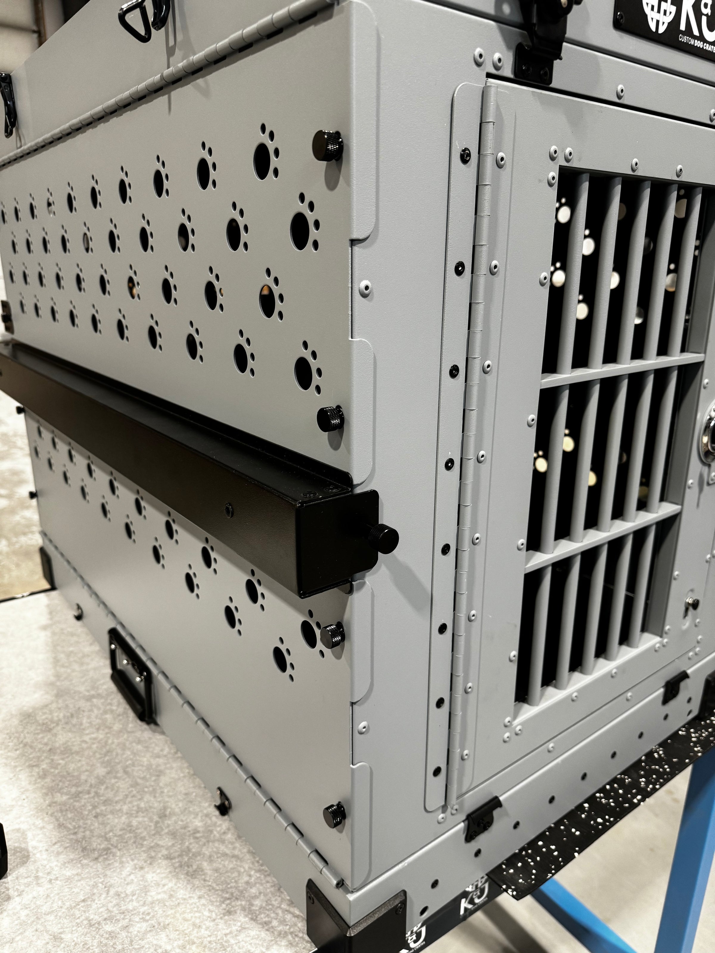 Large grey collapsible K&J crate shown at an angle, highlighting the security side screws for added reinforcement and stability. Crate set in an industrial warehouse