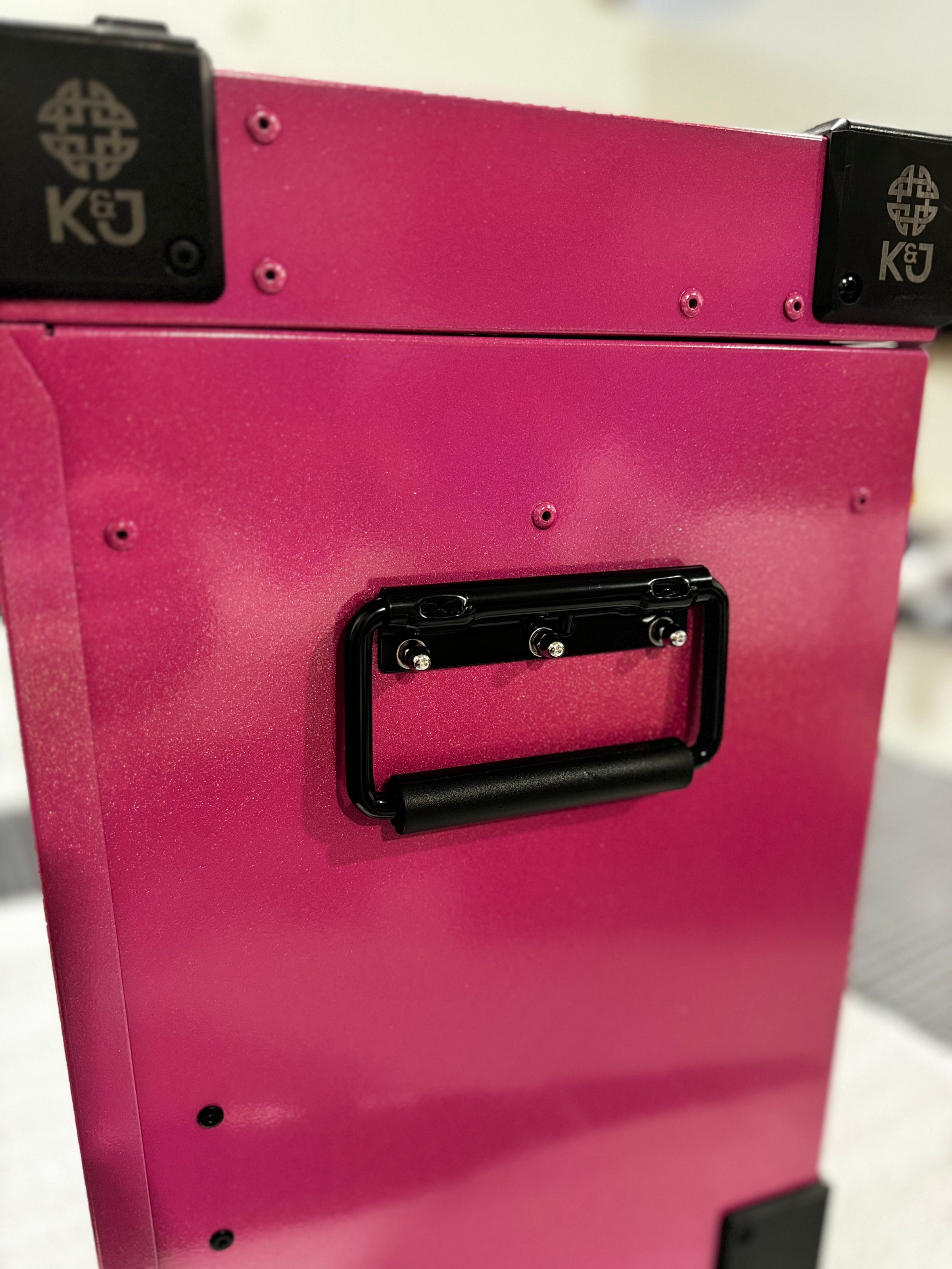 Close-up of the spring-loaded side handle on a small K&J tack box with a pink metallic Glitterazzi powder coat, inside a workshop.