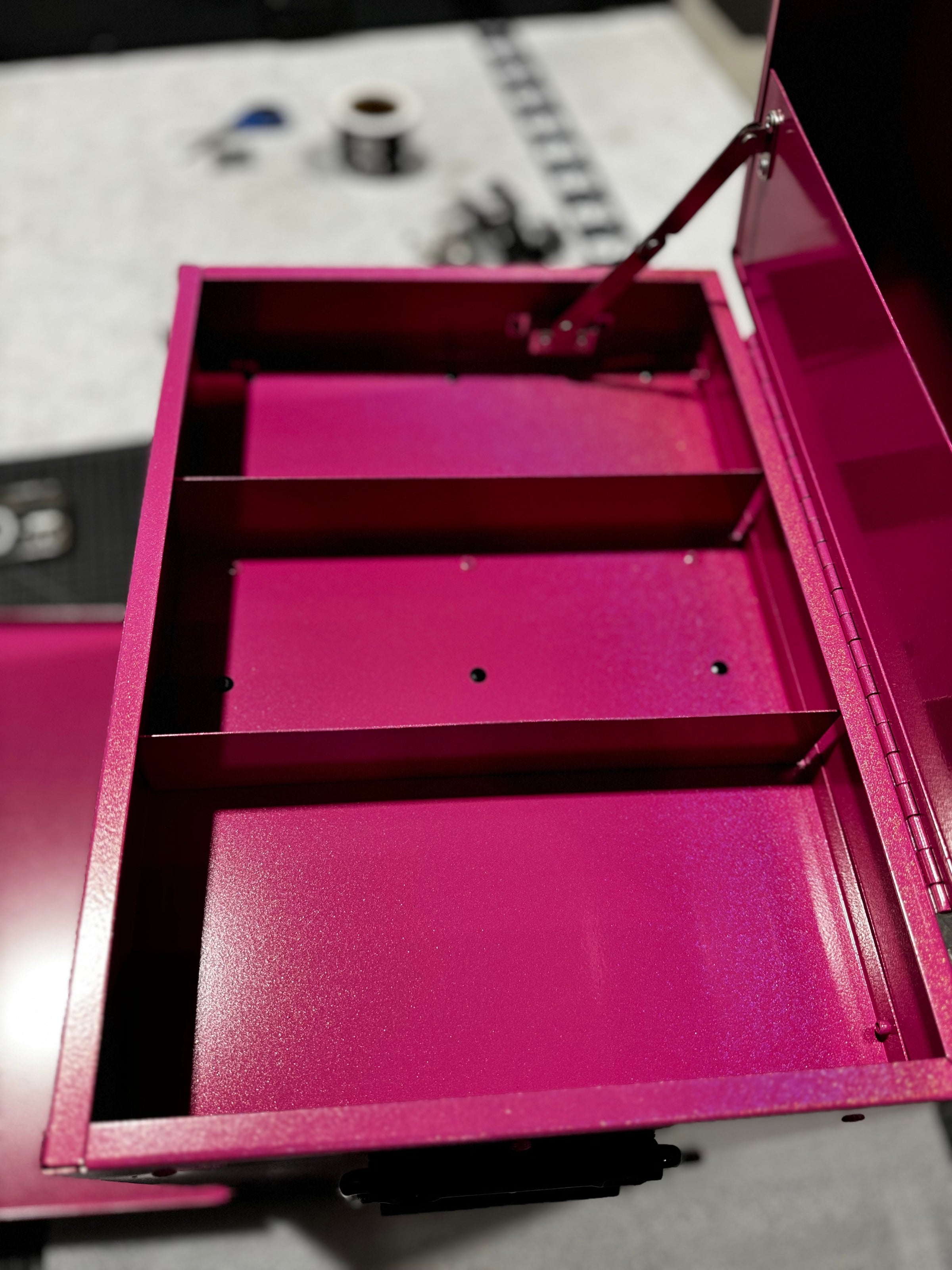 Small K&J tack box with a pink metallic Glitterazzi powder coat, showcasing the top storage section with three separate compartments. Sitting on a table in a workshop.